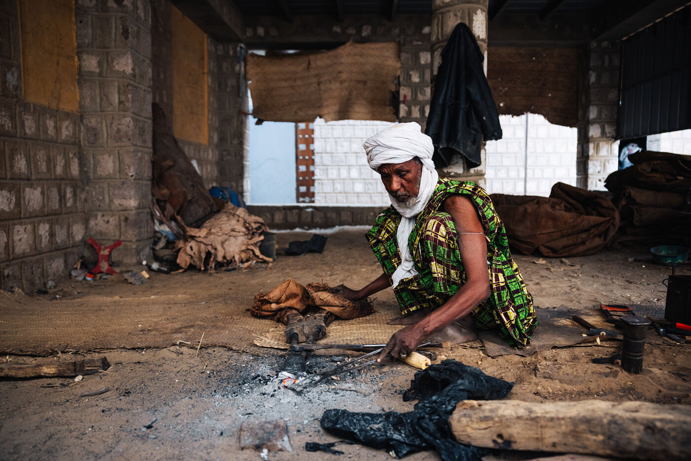 Turbaned craftsman working over embers with hand tools in an open-sided workshop