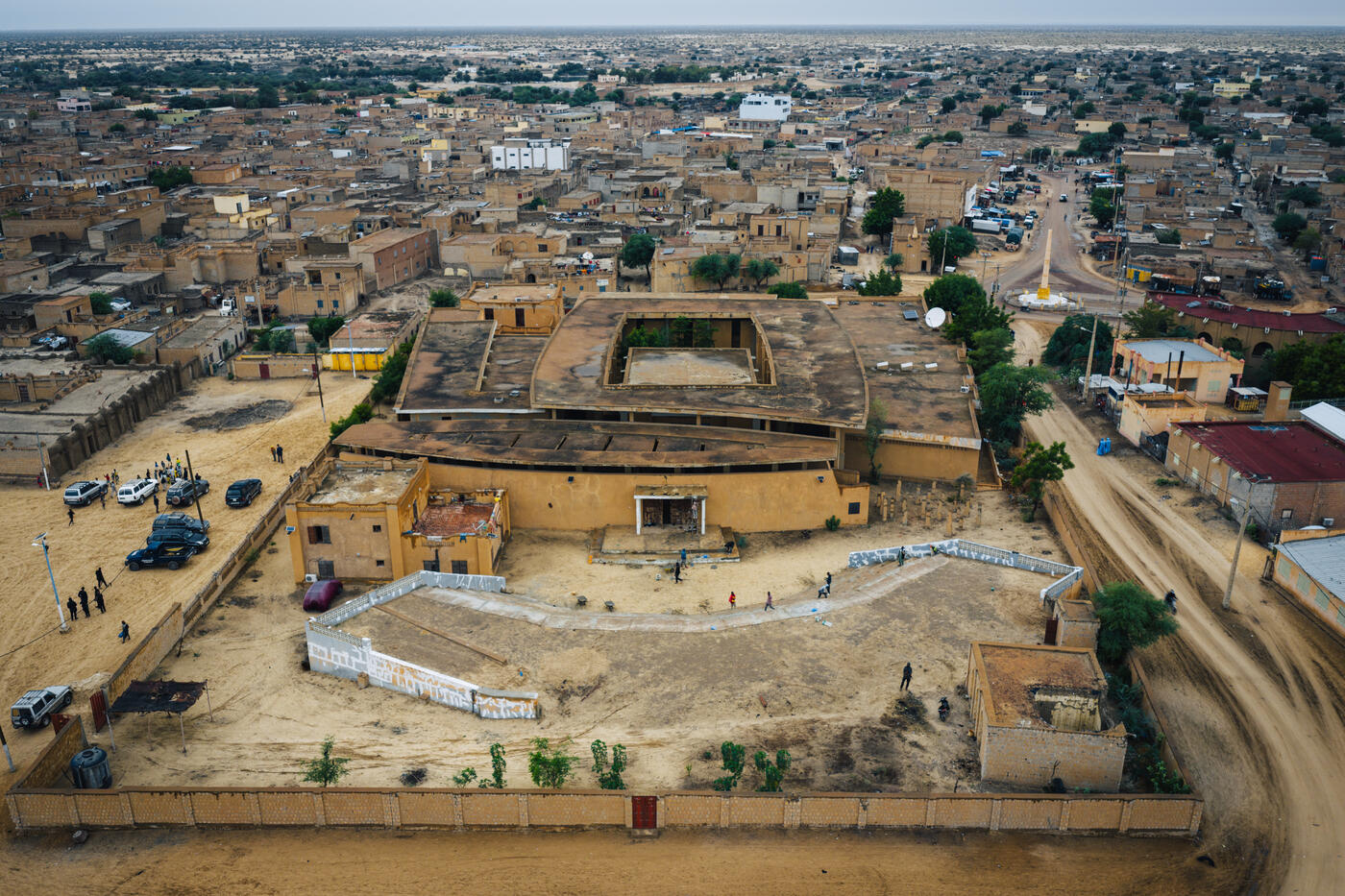 Aerial view of the Ahmed Baba Institute's curved courtyard and walled compound, with escort vehicles parked outside