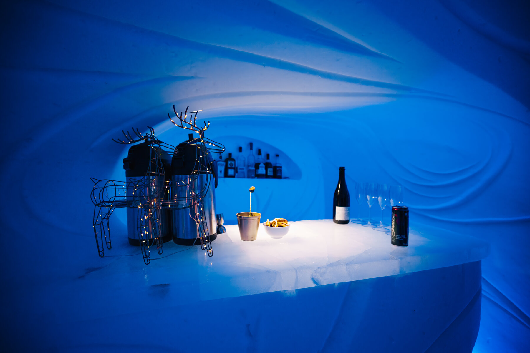 Ice bar at Wolf's Fang with antler-decorated reindeer figures, wine bottles, and glasses on a glowing ice counter