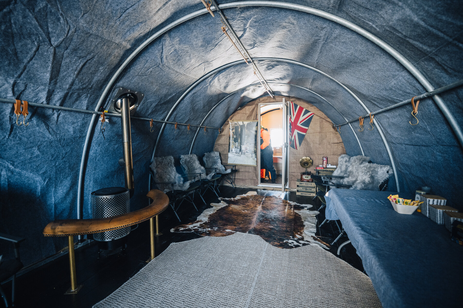 Interior of the Wolf's Fang canvas lounge with blue Union Jack flag, cowhide rug, and fur-draped benches