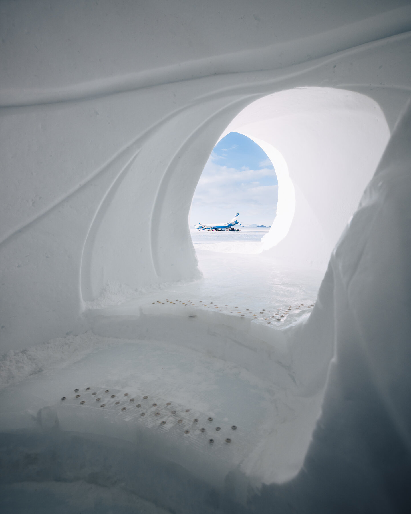 View through a sculpted ice cave opening looking out at the White Desert private jet on the Wolf's Fang runway