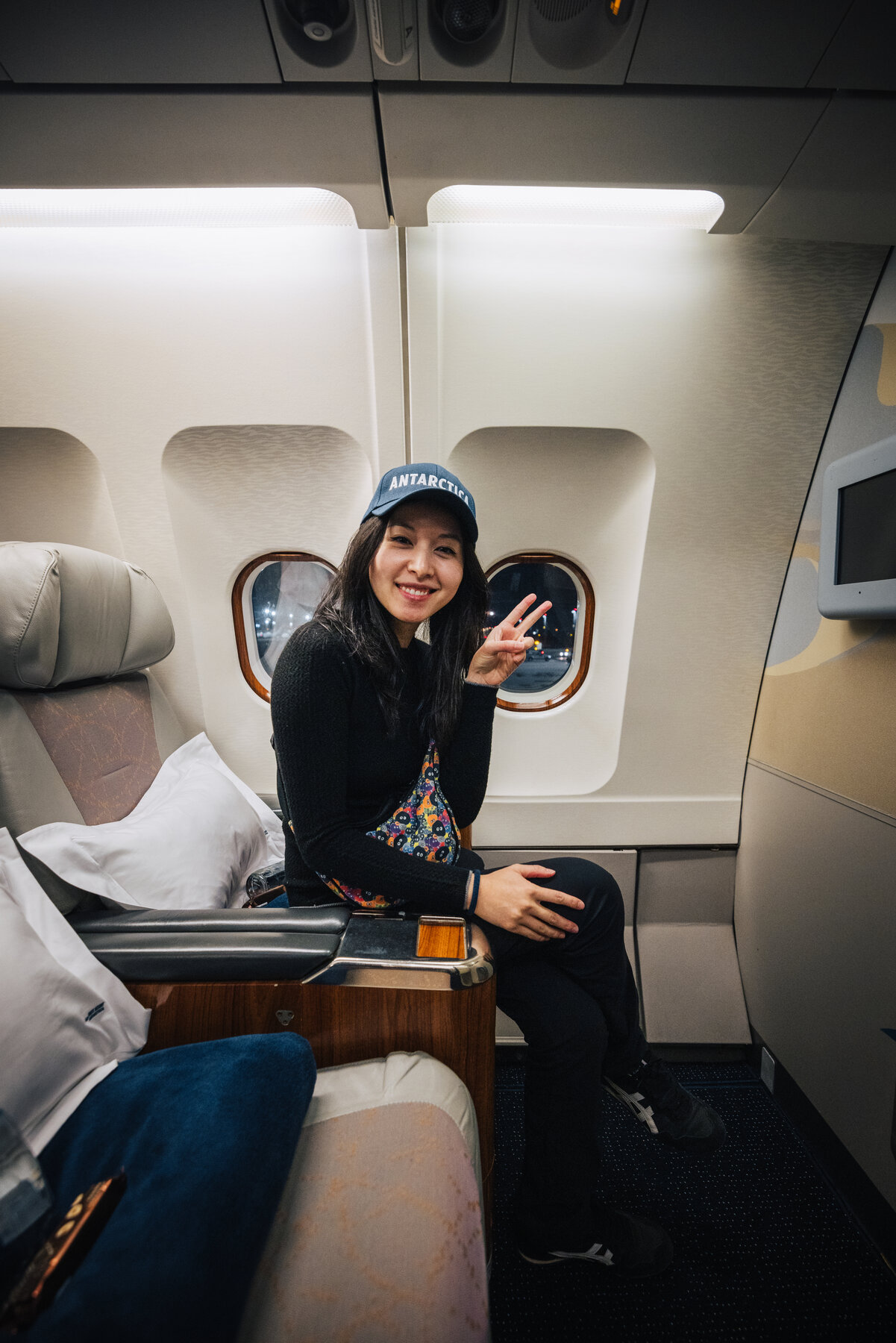 Grace in the private jet cabin wearing an Antarctica cap, smiling and giving a peace sign