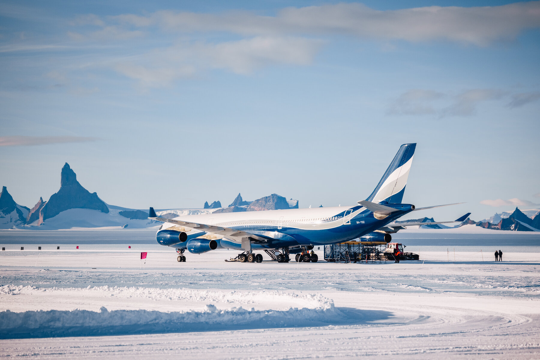 Blue and white private jet parked on the blue ice runway with jagged Wolf's Fang nunatak peaks in the background