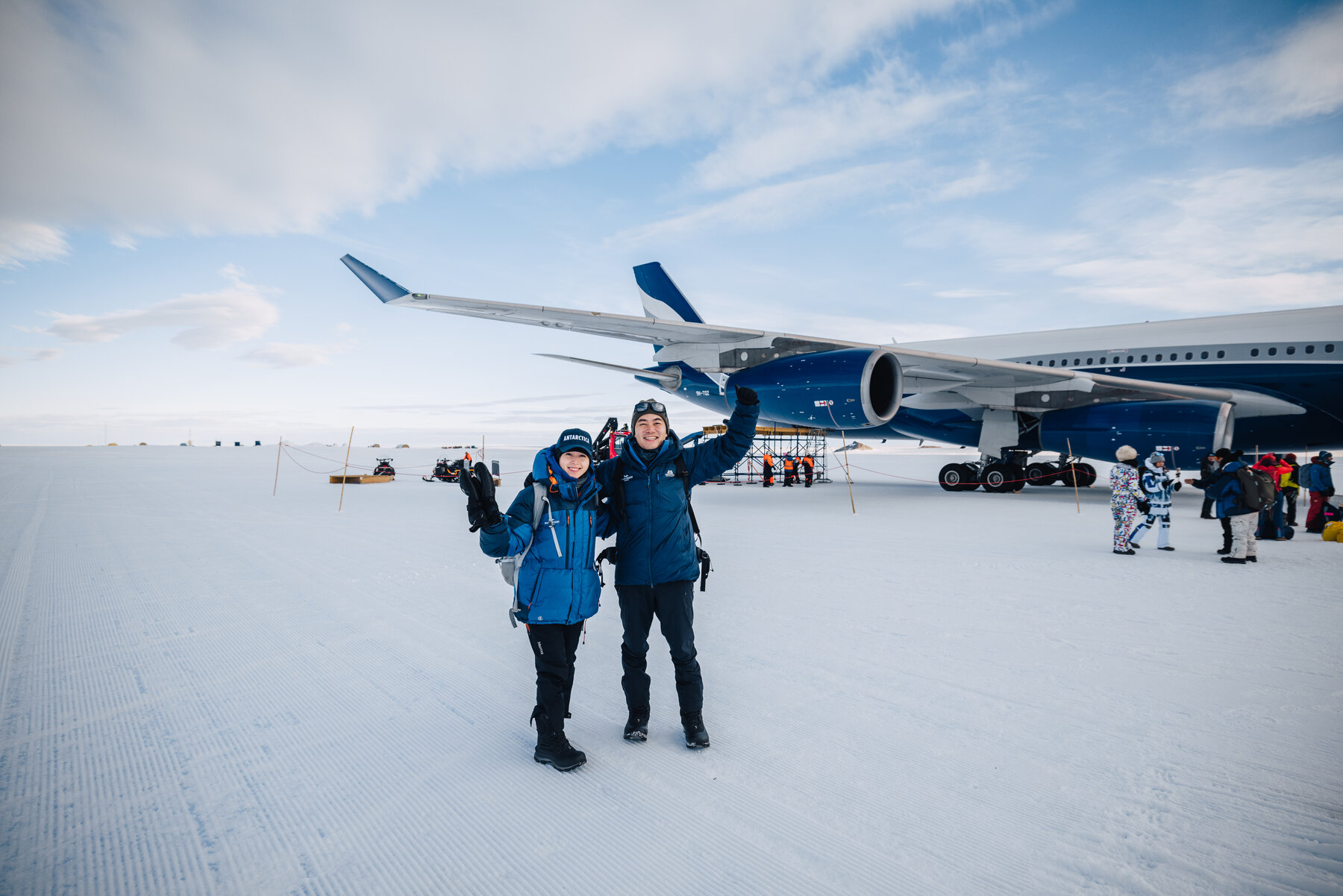 Jason and Grace standing in winter parkas on the ice runway in front of the parked private jet