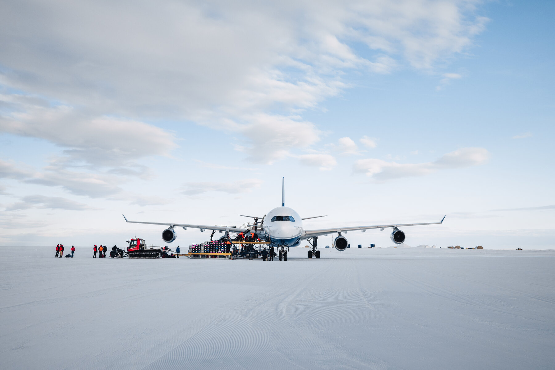 Head-on wide shot of the White Desert A340 private jet parked on the blue ice runway with crew unloading supplies