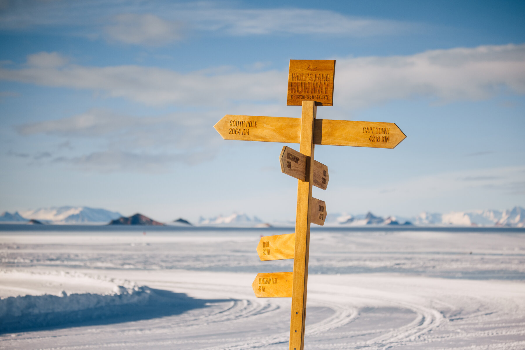 Yellow wooden directional signpost reading Wolf's Fang Runway with arrows to South Pole 2064 km and Cape Town 4398 km