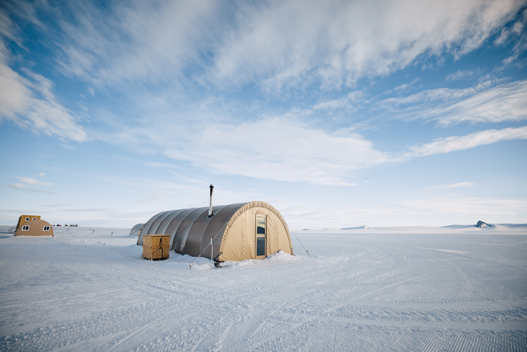 Exterior of a Wolf's Fang canvas Quonset tent on the Antarctic plateau under a blue sky