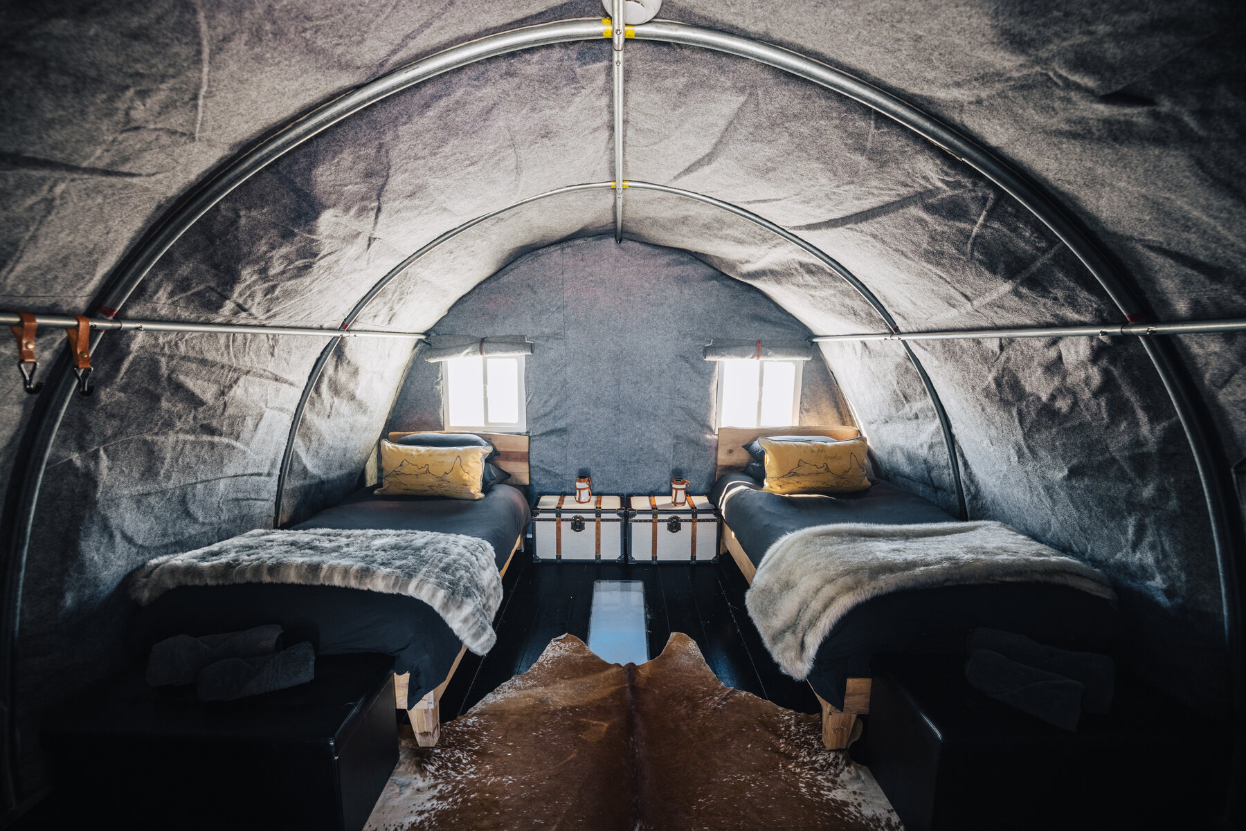 Wolf's Fang sleeping tent interior with two twin cots, yellow pillows, fur throws, and a shared wooden trunk between them