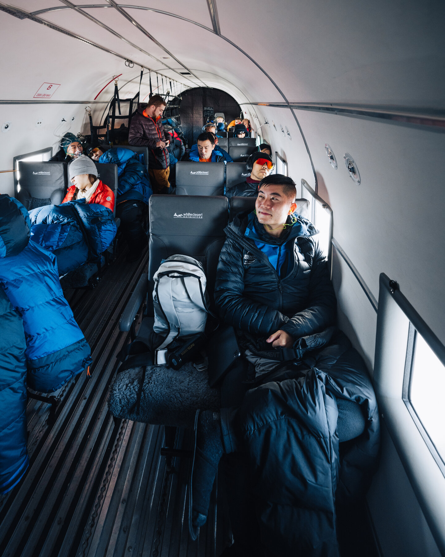 Passengers in heavy blue and orange parkas seated in the unpressurized cabin of the Basler BT-67 during the flight to the South Pole