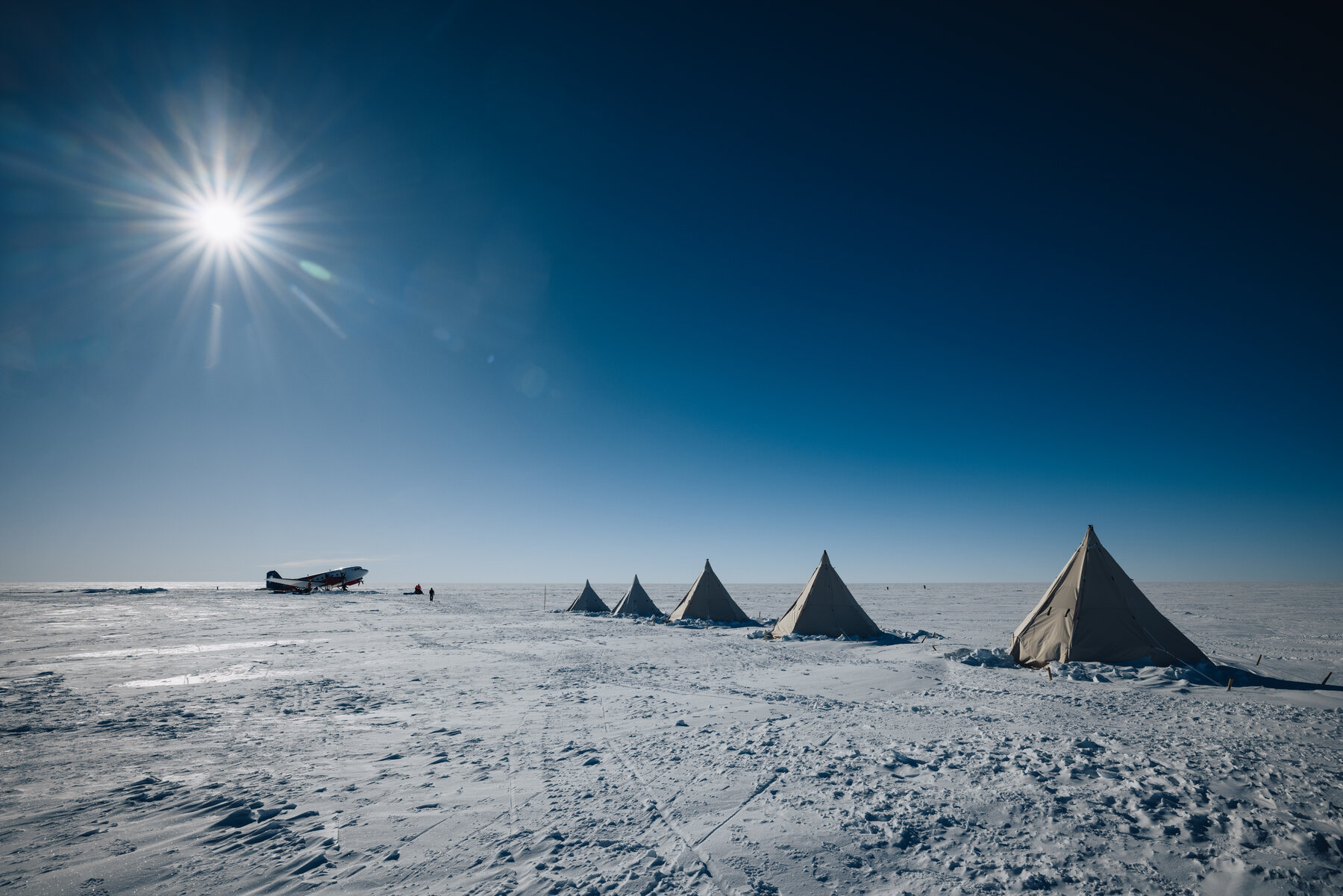 Row of white canvas teepee tents at Dixie's Camp spread across the empty polar plateau under a deep blue sky
