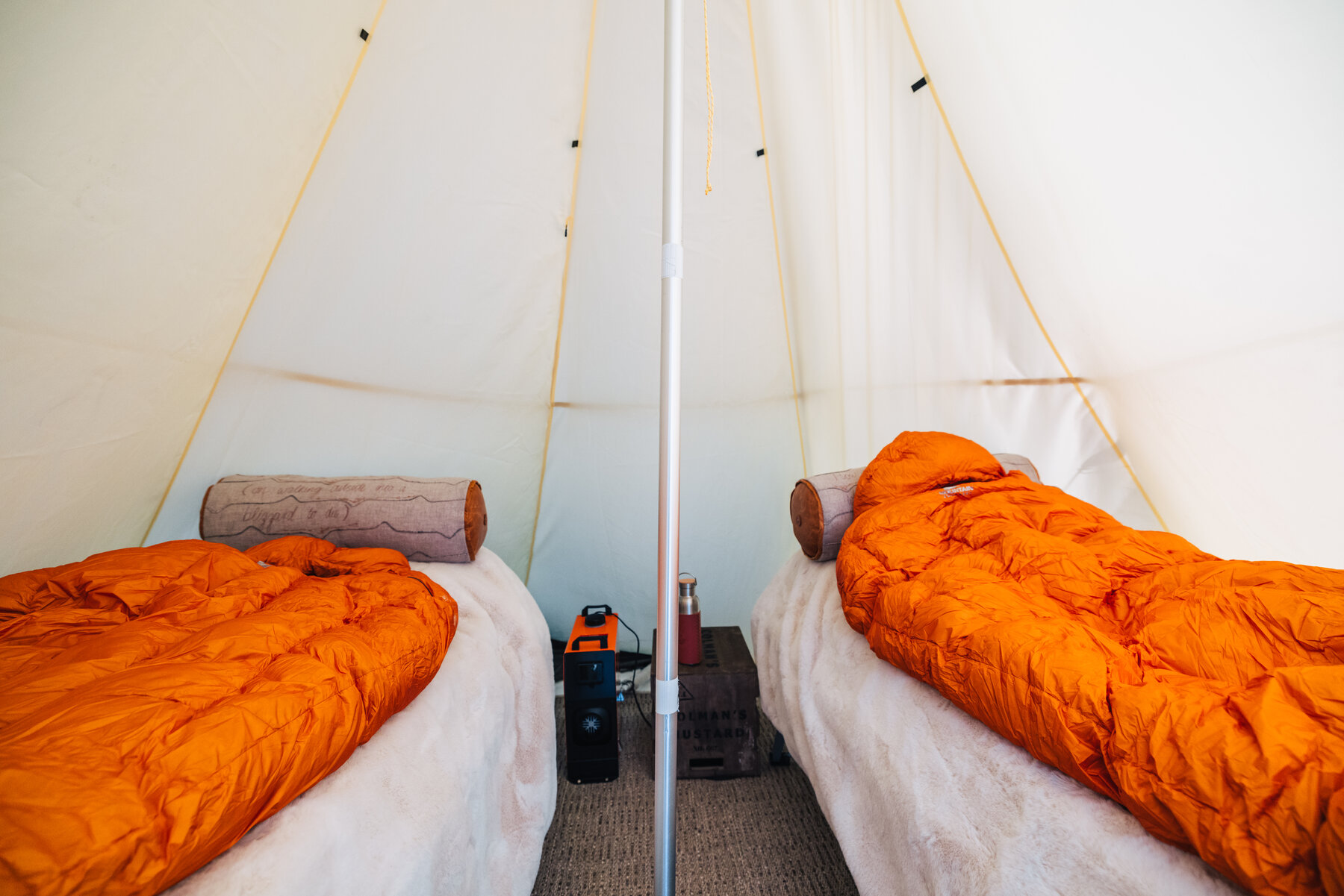 Interior of a Dixie's Camp teepee with orange sleeping bags on two twin cots, white canvas walls, and a central wooden pole