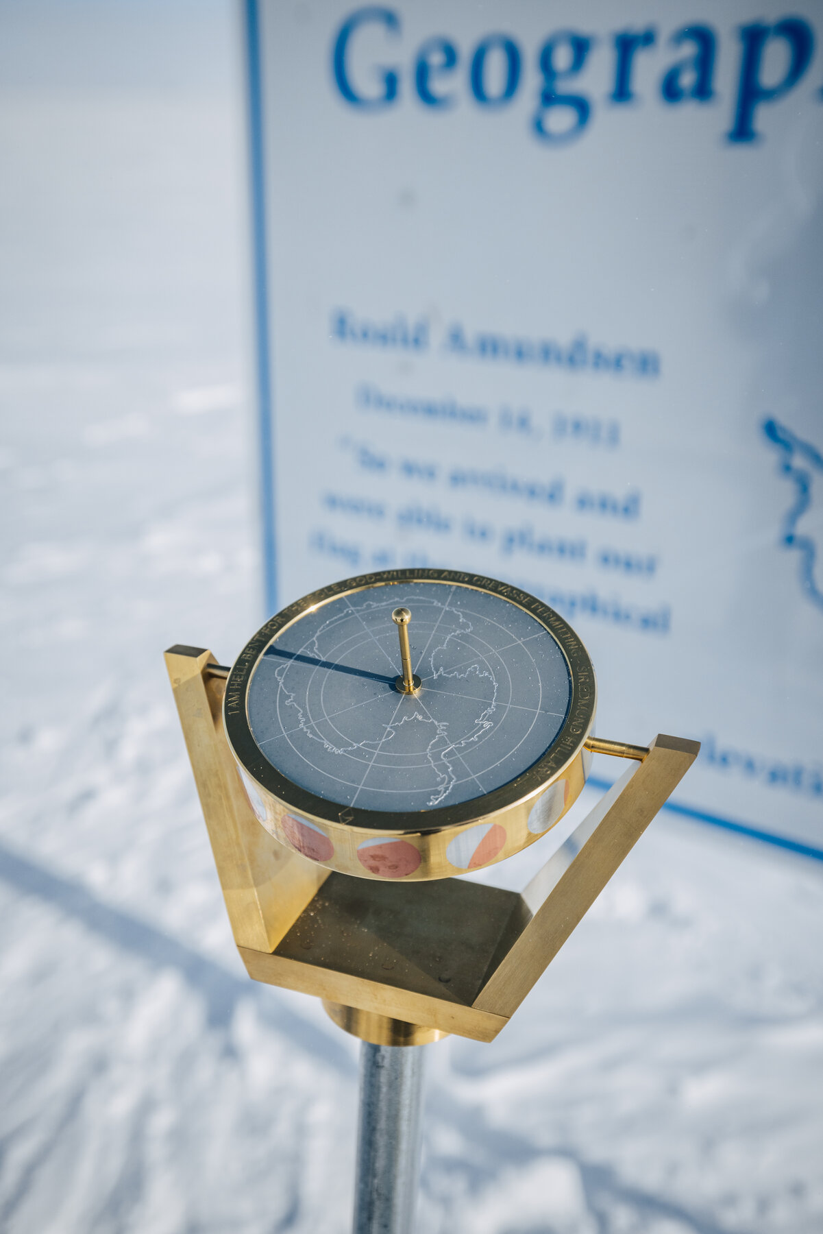The small brass Geographic South Pole marker and compass mounted on the ice at 90 degrees south