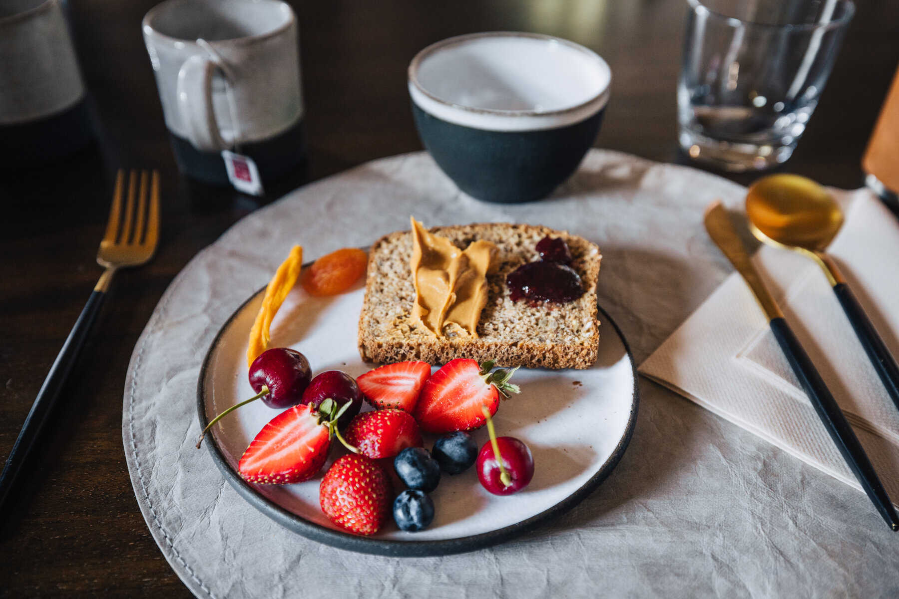 Breakfast plate at Whichaway with seeded toast topped with peanut butter and jam and a side of fresh strawberries, blueberries, and cherries