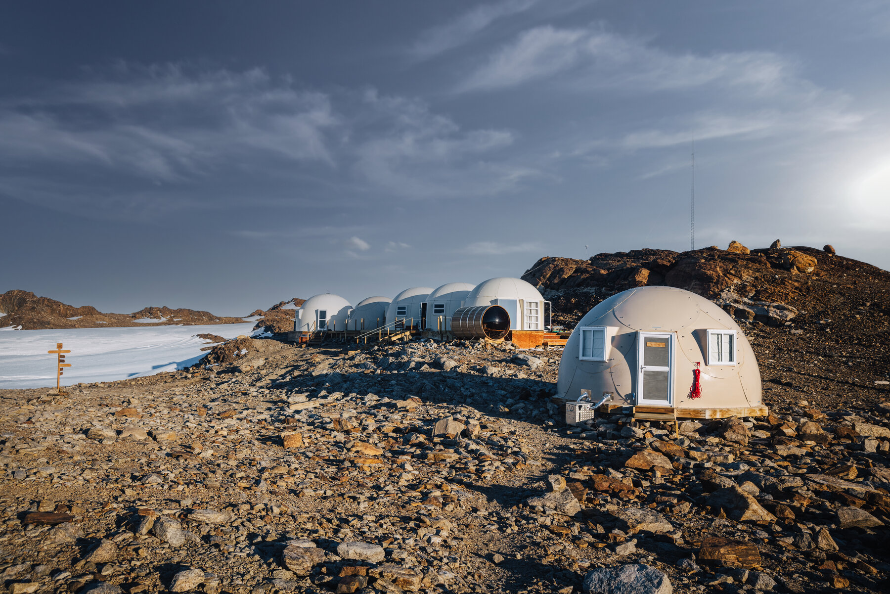 Row of Whichaway dome pods lined up across the rocky outcrop in golden afternoon light with the frozen lake behind