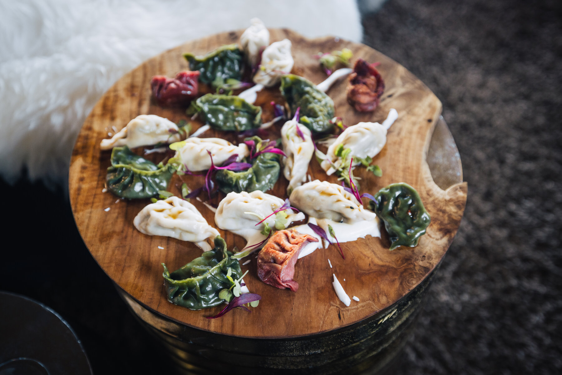 Plated dumpling course on a wooden slab with sauce and purple micro-herbs at the Whichaway dining pod