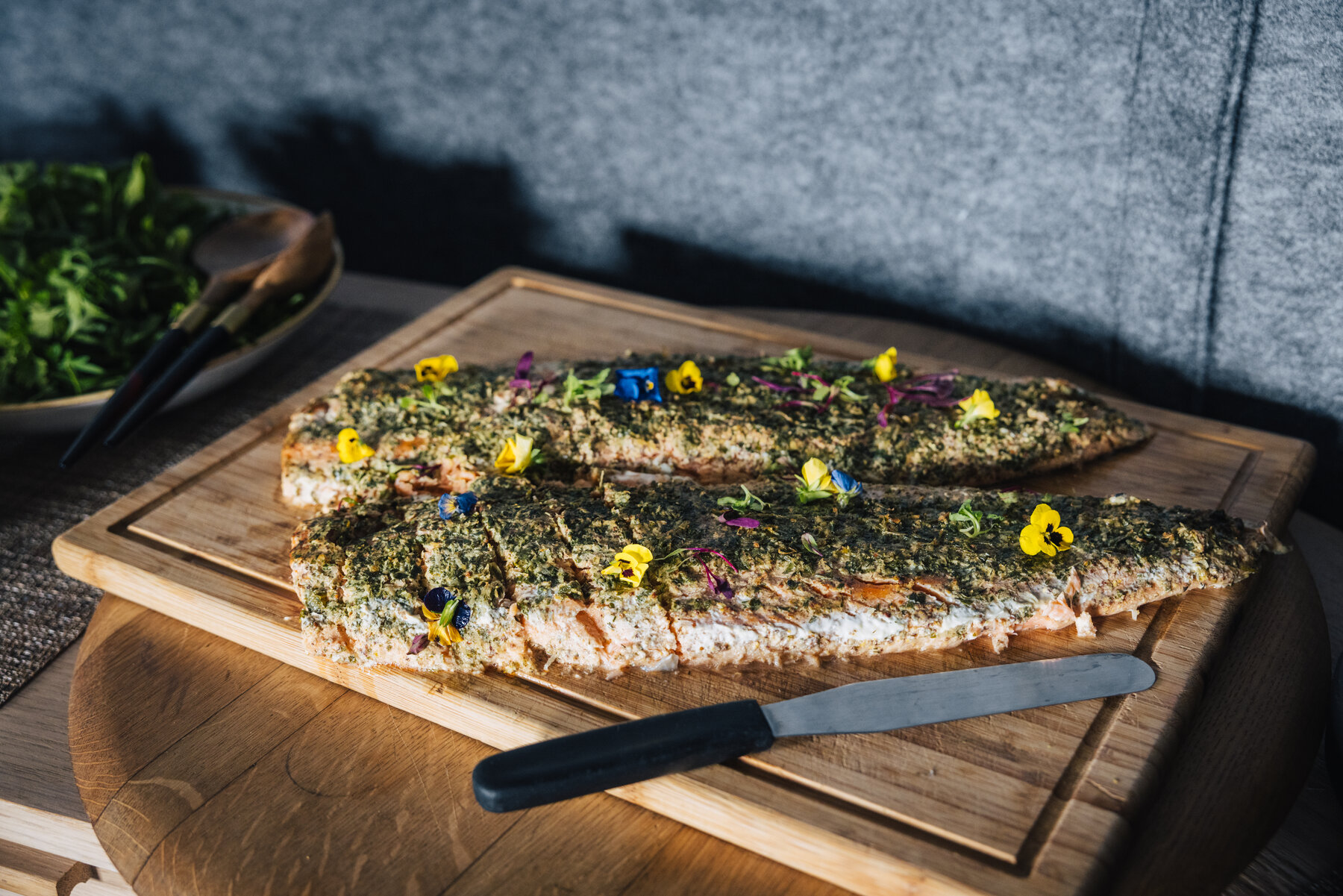 Two herb-crusted salmon fillets on a wooden board garnished with edible flowers ready to be plated at Whichaway