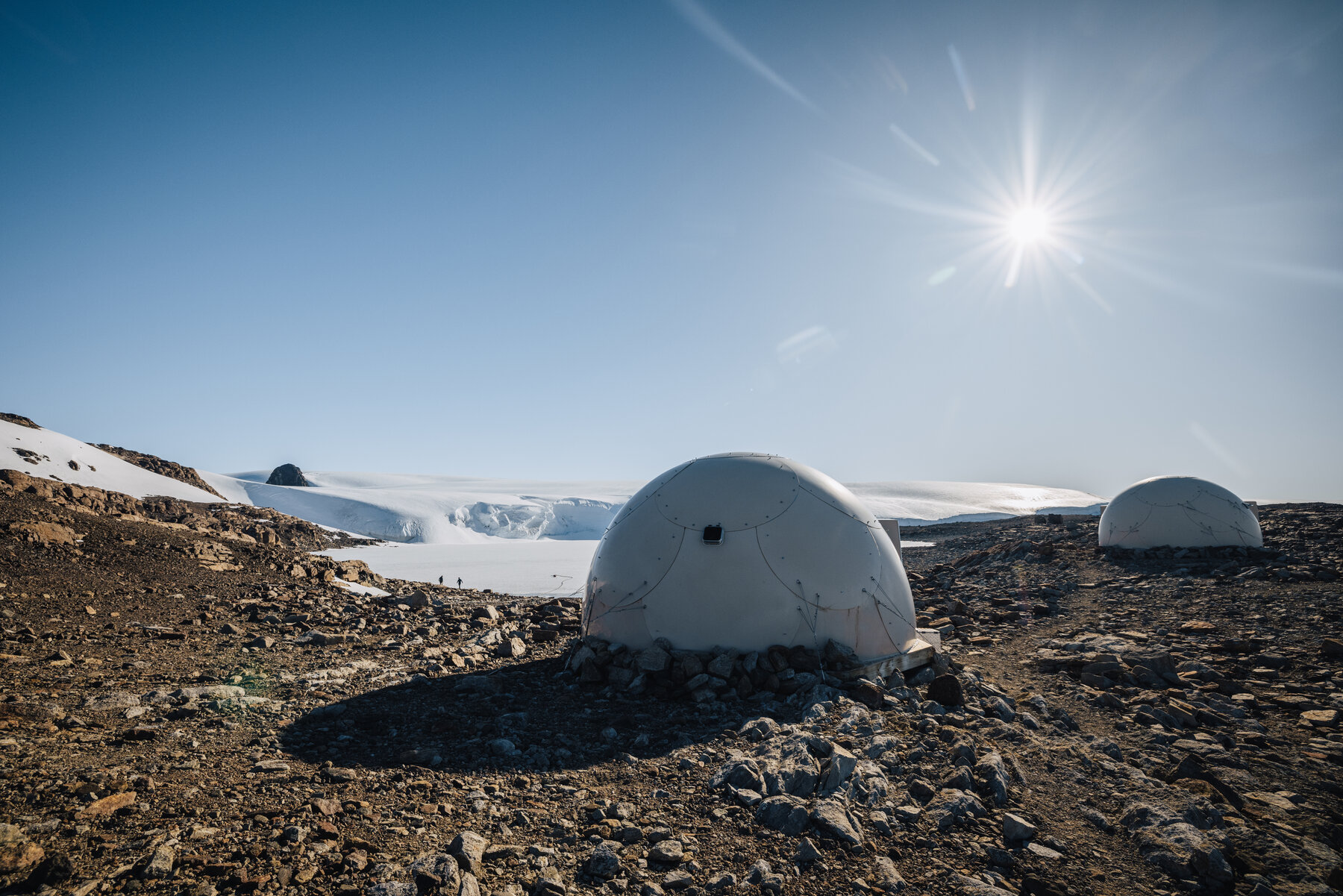 White dome pod at Whichaway catching a bright sun flare overhead with the glacier and frozen lake in the background