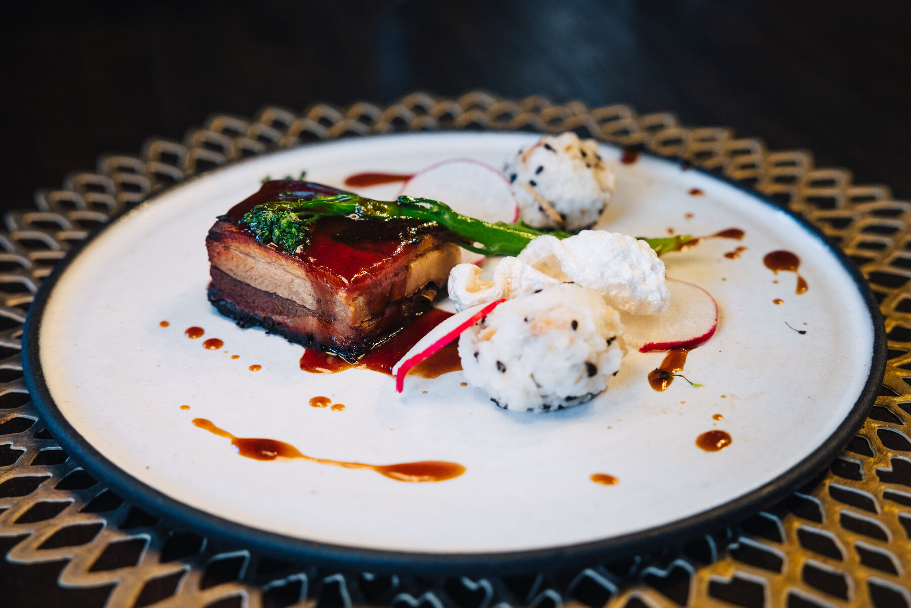 Elegantly plated pork belly with crackling, broccolini, radish, and sesame rice balls on a white plate at Whichaway