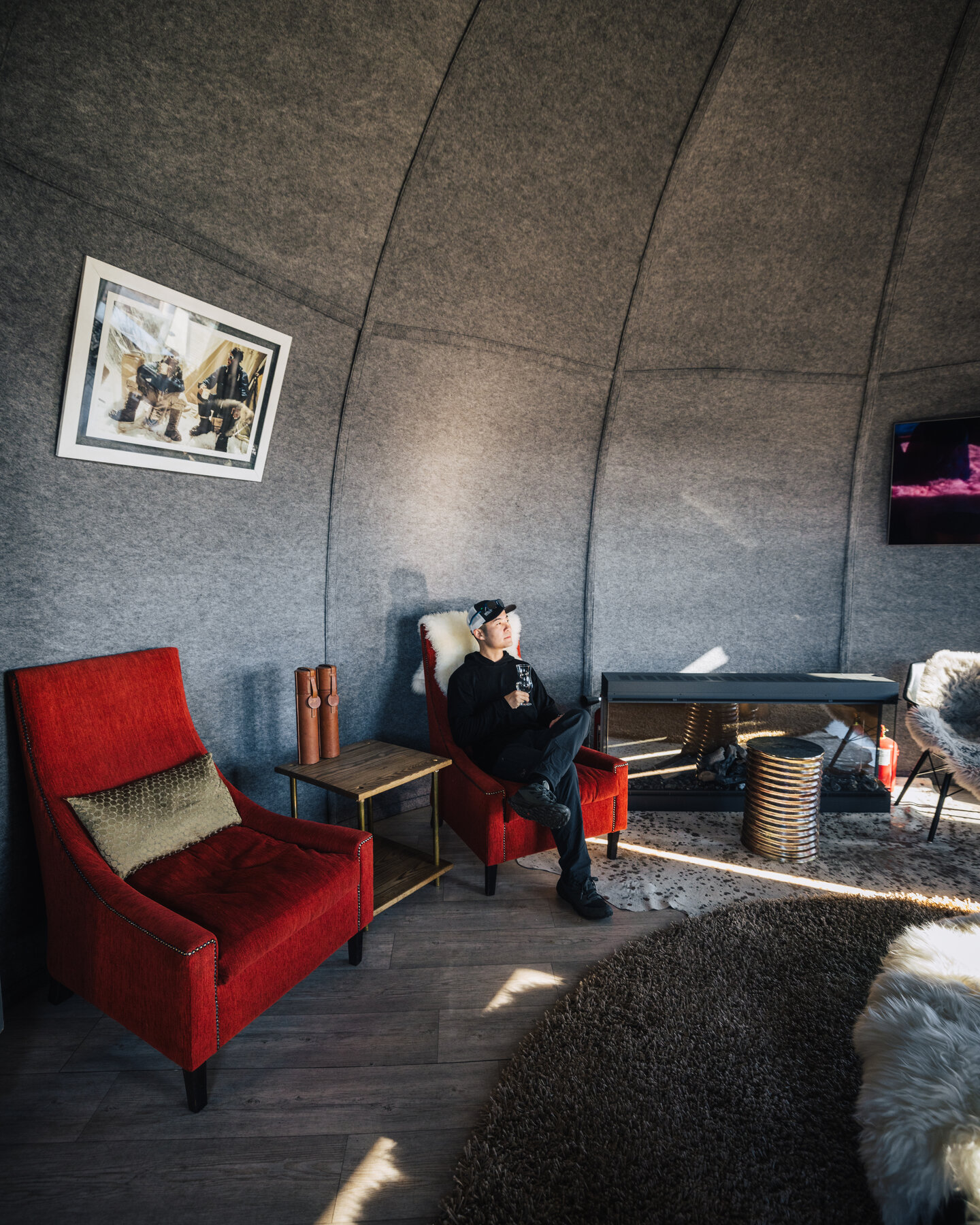 Jason seated in one of the red velvet lounge chairs in the Whichaway reading area with framed polar photography on the wall behind