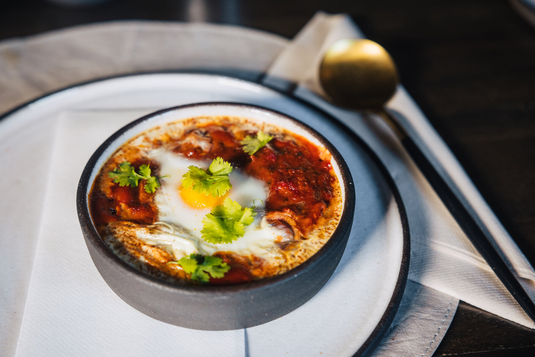 Shakshuka served in a small cast iron dish with a baked egg, tomato sauce, mushrooms, and fresh cilantro at Whichaway