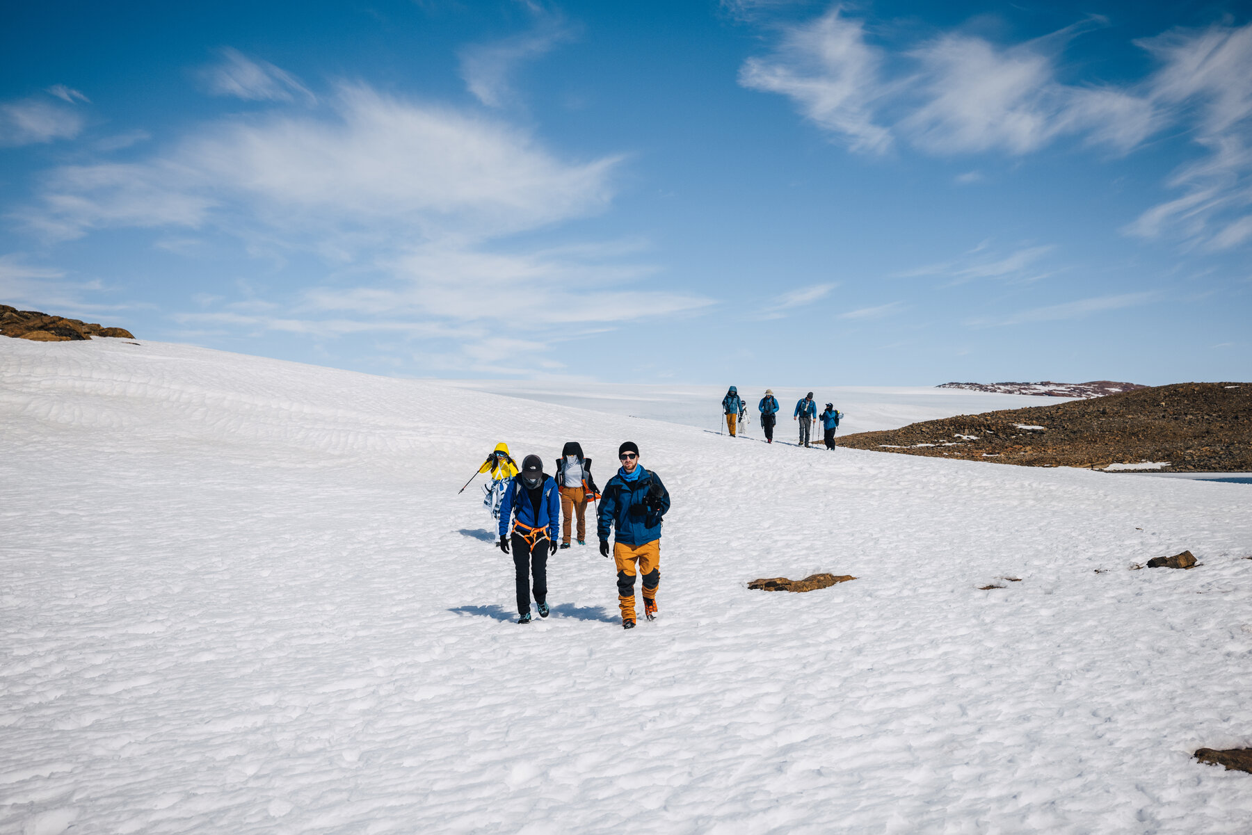 Group of travelers in heavy parkas hiking together across a wide Antarctic snowfield
