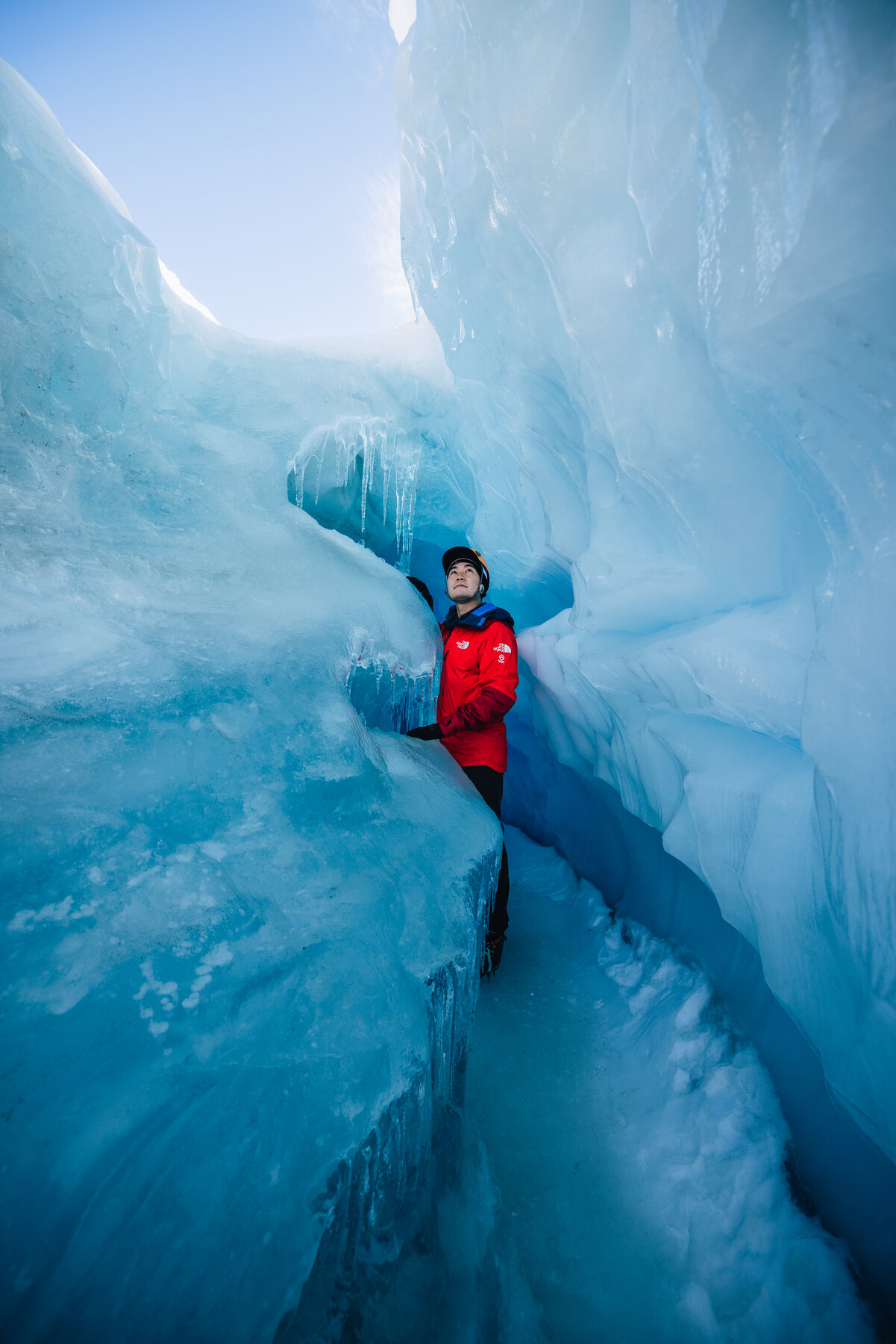 Jason looking up toward the light through a narrow slot in a blue ice crevasse