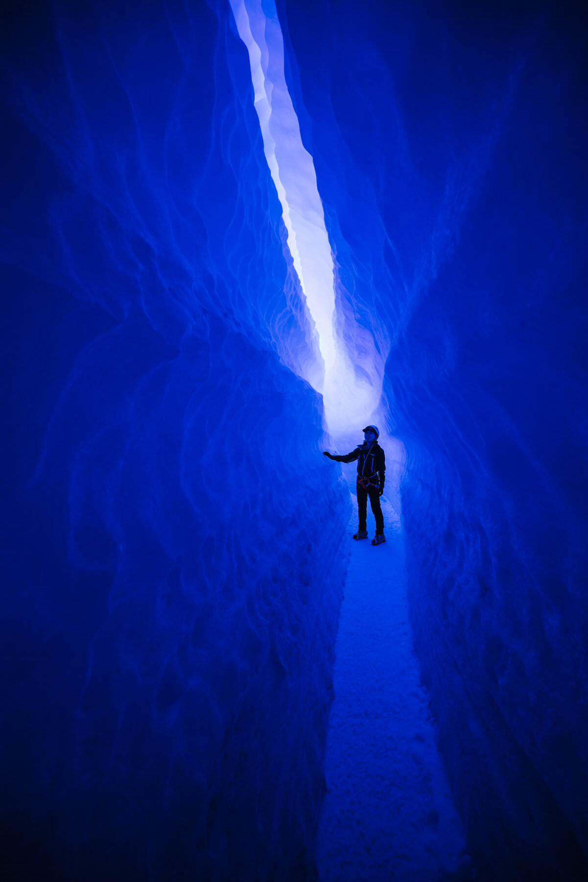 Silhouette of a climber reaching upward toward the light inside a deep blue ice crevasse