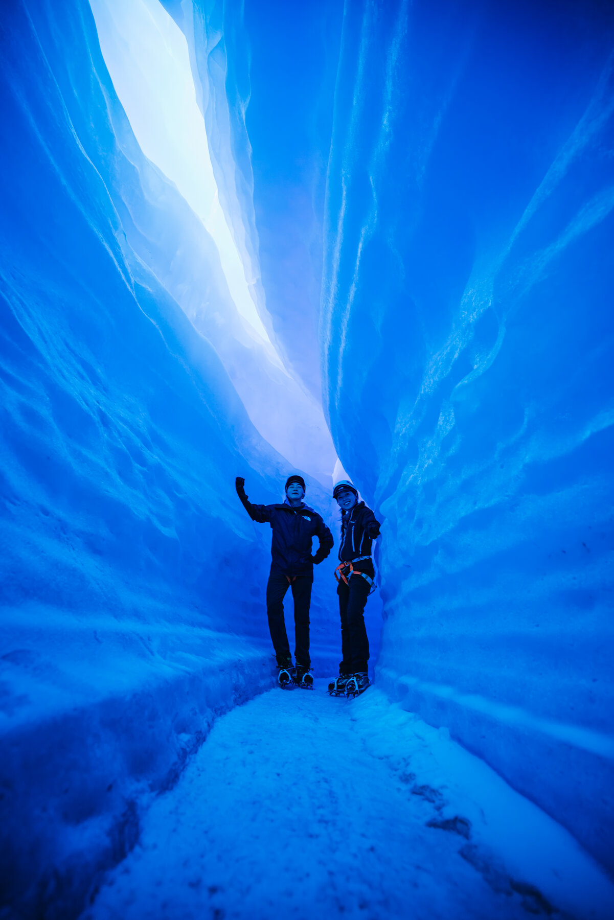 Jason and Grace together inside the blue glacial ice tunnel wearing yellow climbing helmets