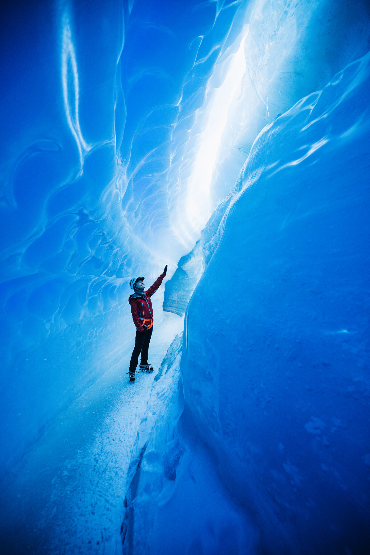 Grace posing against a rippled blue ice wall with sculpted texture from ancient glacial flow