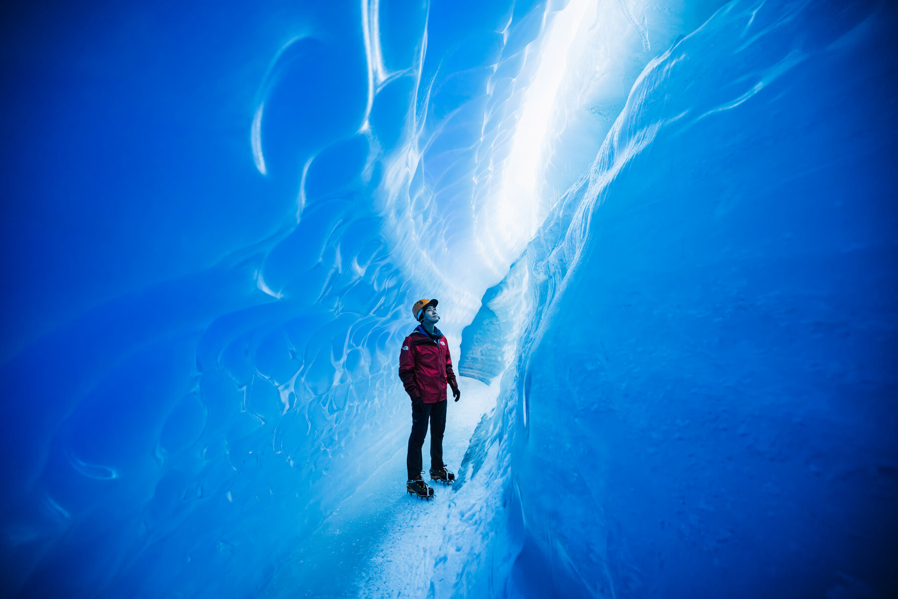 Jason standing against a rippled glacial ice wall with striations of blue and white curving around him