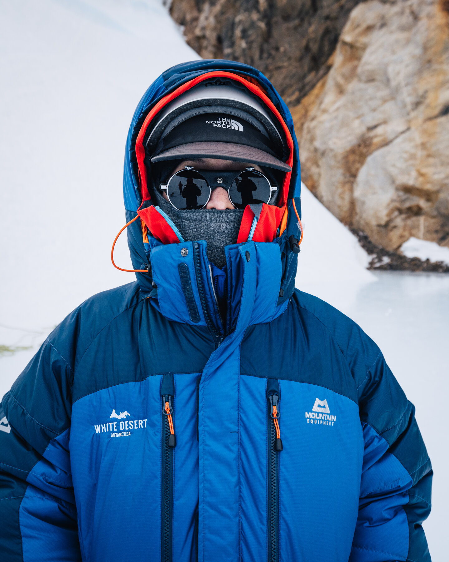 Portrait of a climber fully bundled in a blue White Desert parka with sunglasses and balaclava, cold weather layered to the eyes
