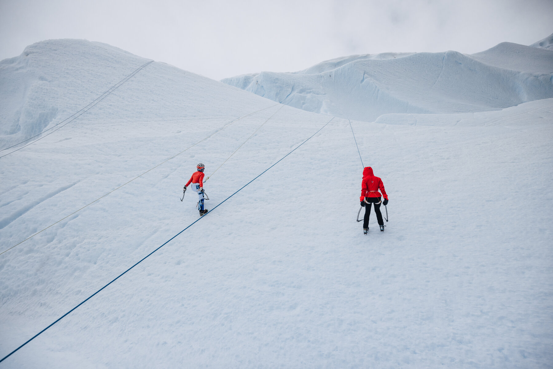Close view of two red-jacketed climbers roped together traversing a snow ridge with ice axes in hand