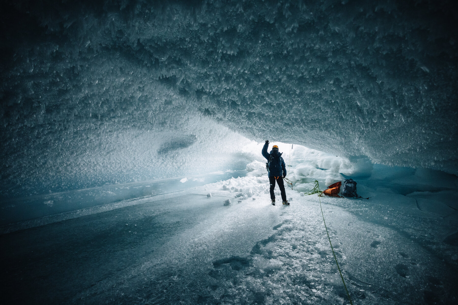 Silhouette of a climber standing inside a cathedral of ice with the crystal-encrusted ceiling curving overhead and daylight pouring in from the entrance