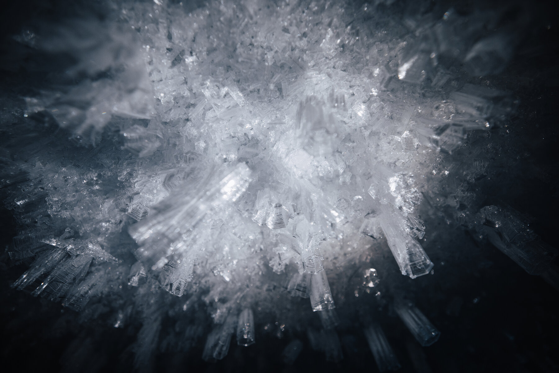 Macro close-up of white ice crystals radiating outward from a central point like a frozen burst of light