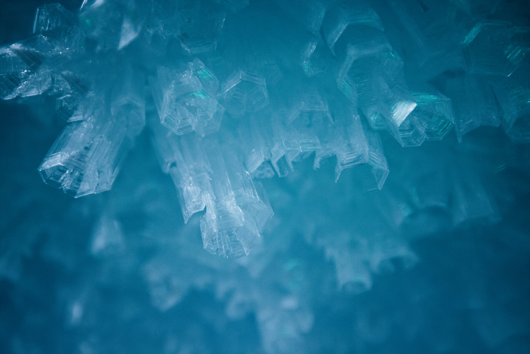 Close-up of hexagonal teal-blue ice crystals clustered together with sharply faceted surfaces