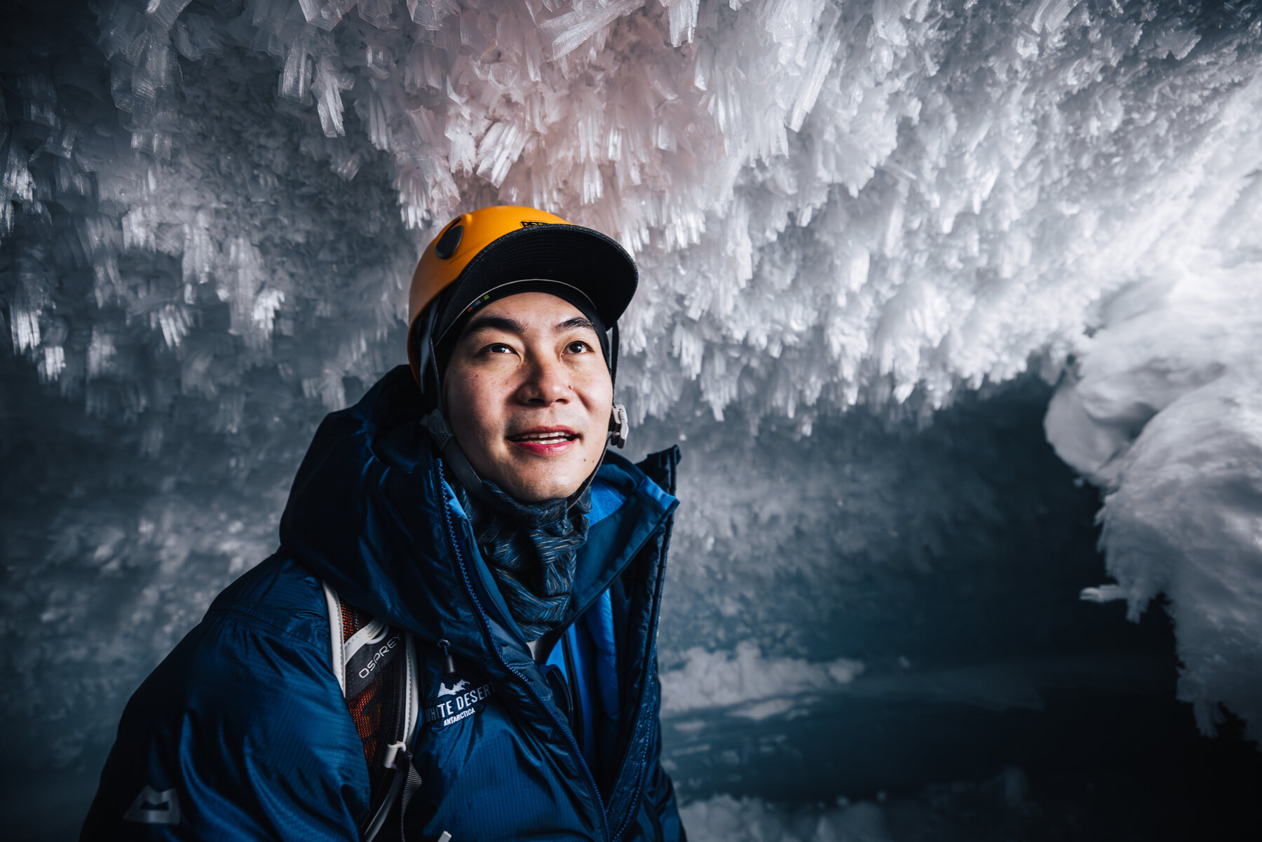Close portrait of Jason in an orange climbing helmet smiling inside the ice cave with crystal ceiling behind him