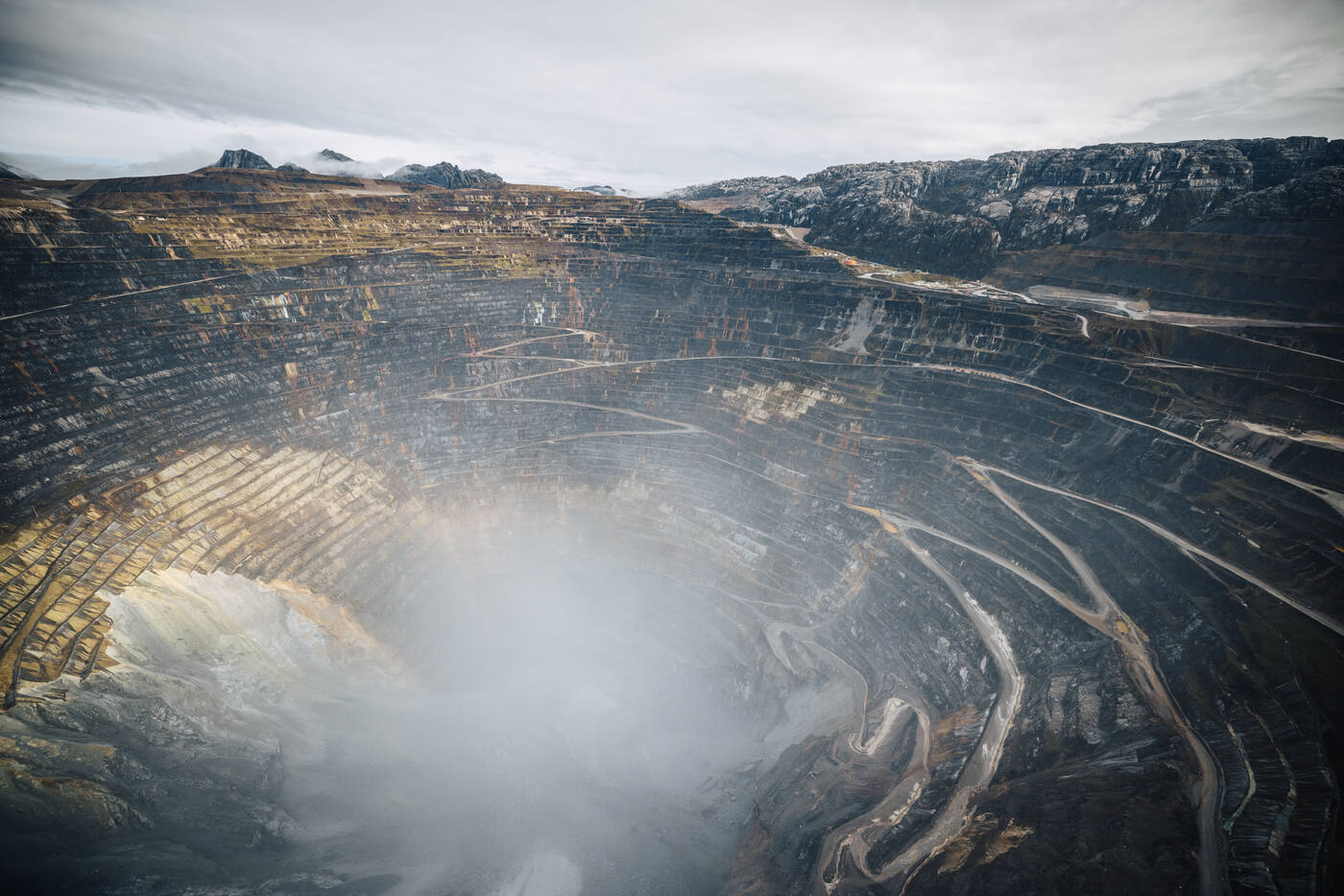 Aerial view down into the terraced open pit of the Grasberg mine, haul roads spiralling into cloud