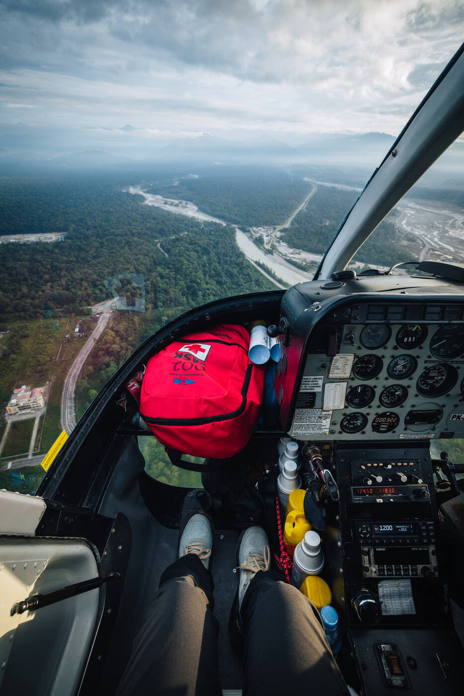 View from inside the helicopter cockpit looking down at a river valley and lowlands of West Papua