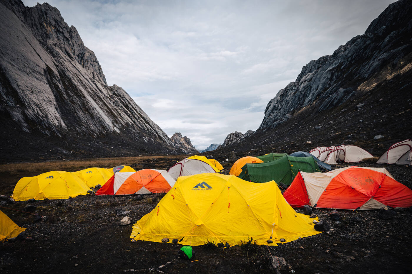 Cluster of yellow, orange and green tents at base camp with limestone walls on either side of the valley