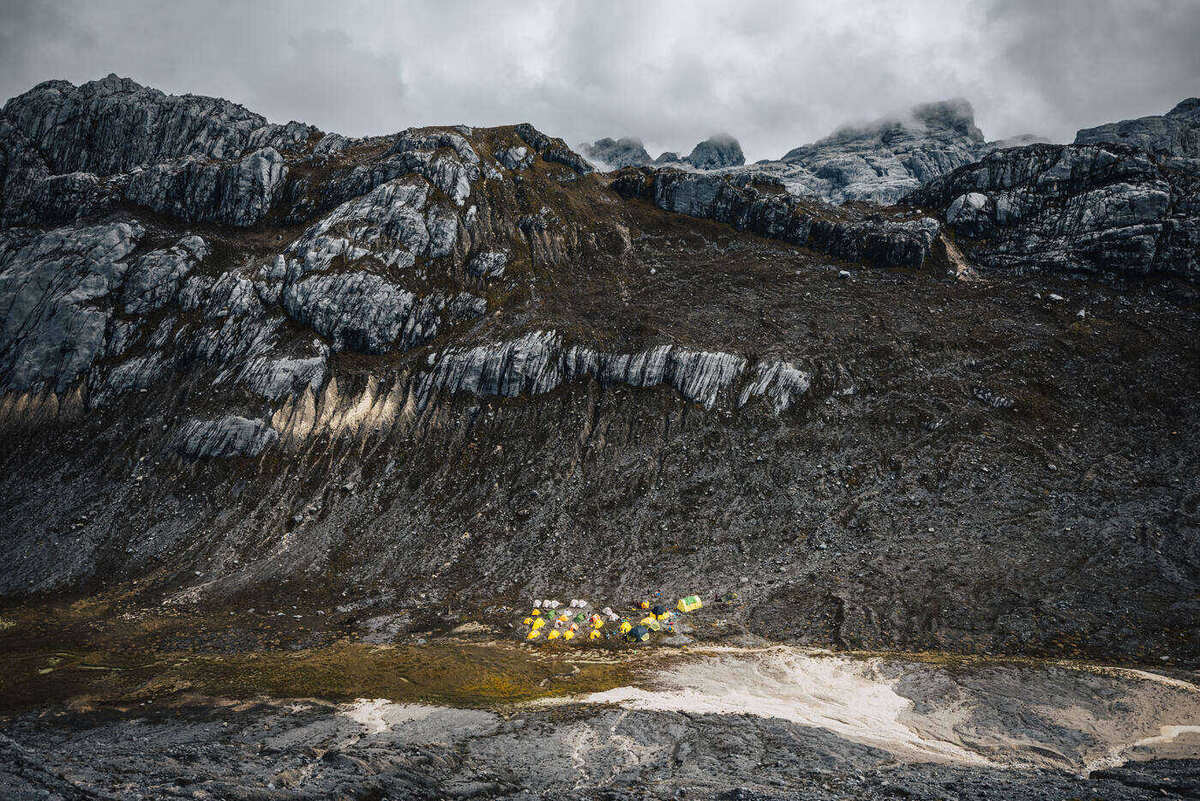 Looking back down over banded limestone slopes to the tiny yellow tents of base camp on the valley floor