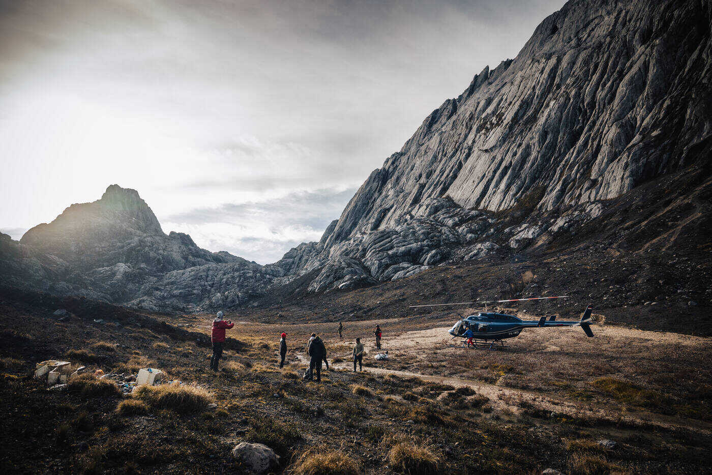 Helicopter landed on the grassy valley floor at base camp with team members gathered and limestone walls rising behind
