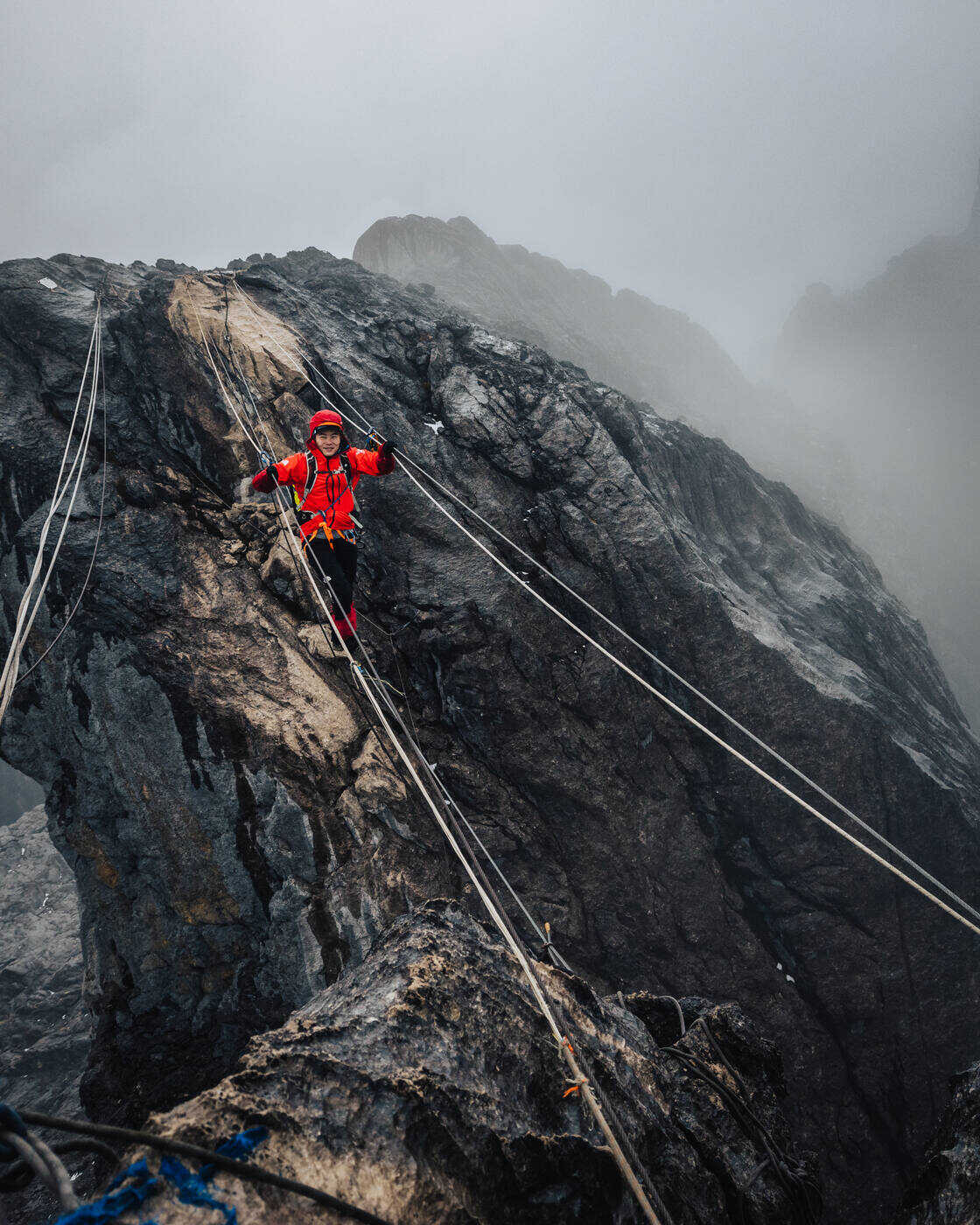 Climber in red jacket on dark limestone formation at summit