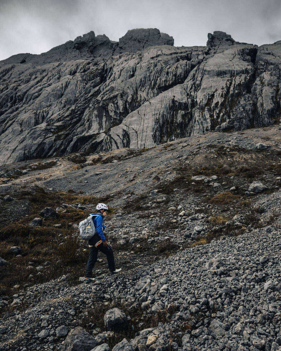 Single climber ascending loose scree toward cliff faces in exposed mountain terrain
