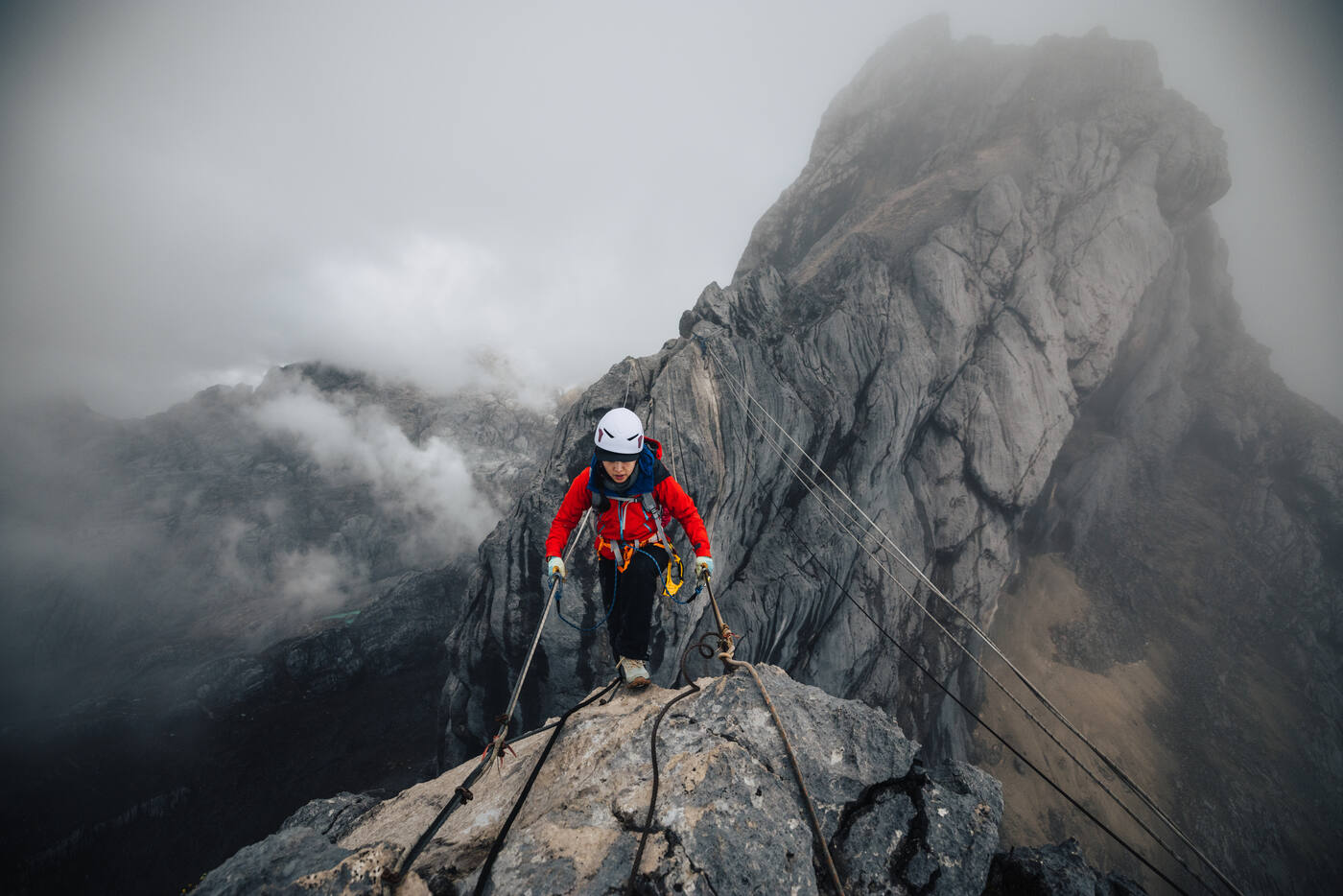 Climber in red on columnar rock wall in dense fog