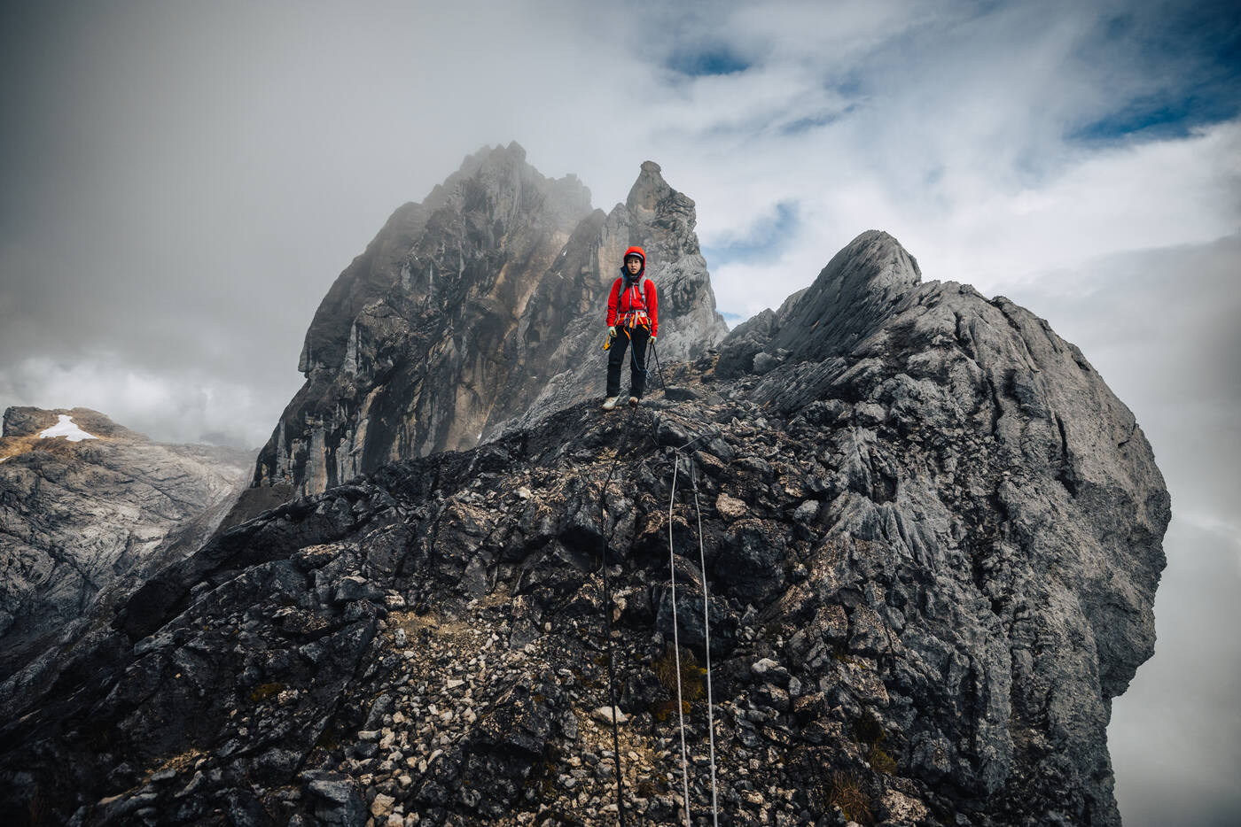 Climber on summit with multiple rock formations and rope visible
