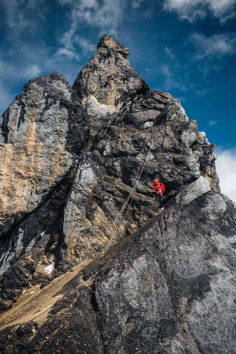 Climber in red gear on steep columnar limestone with deep blue sky behind