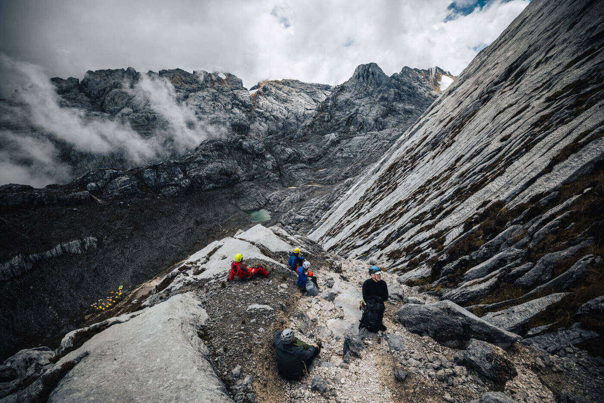 Multiple climbers traversing wide rock formation with steep mountain walls