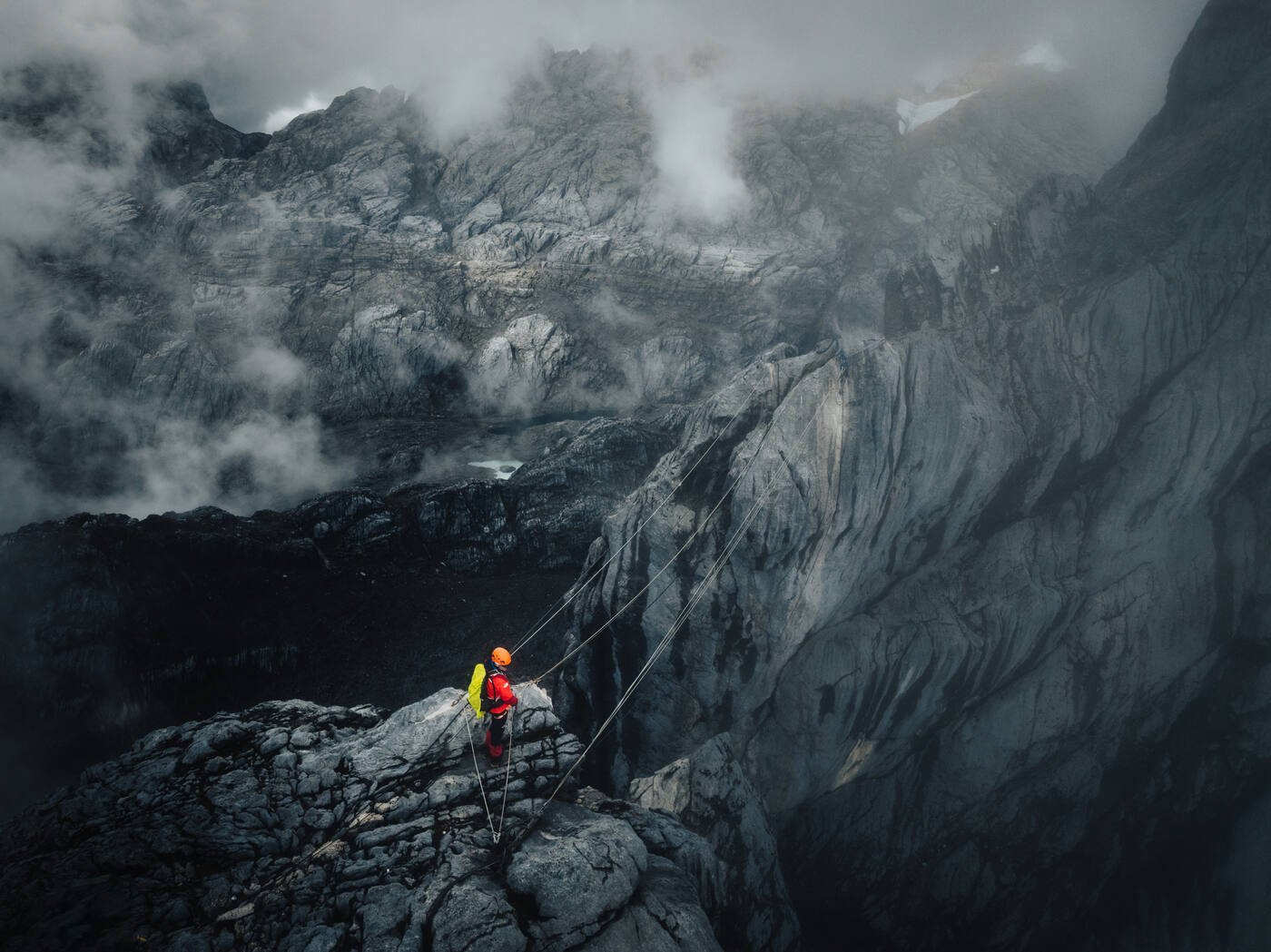 Drone shot of climber on rock wall with rope and misty valley below