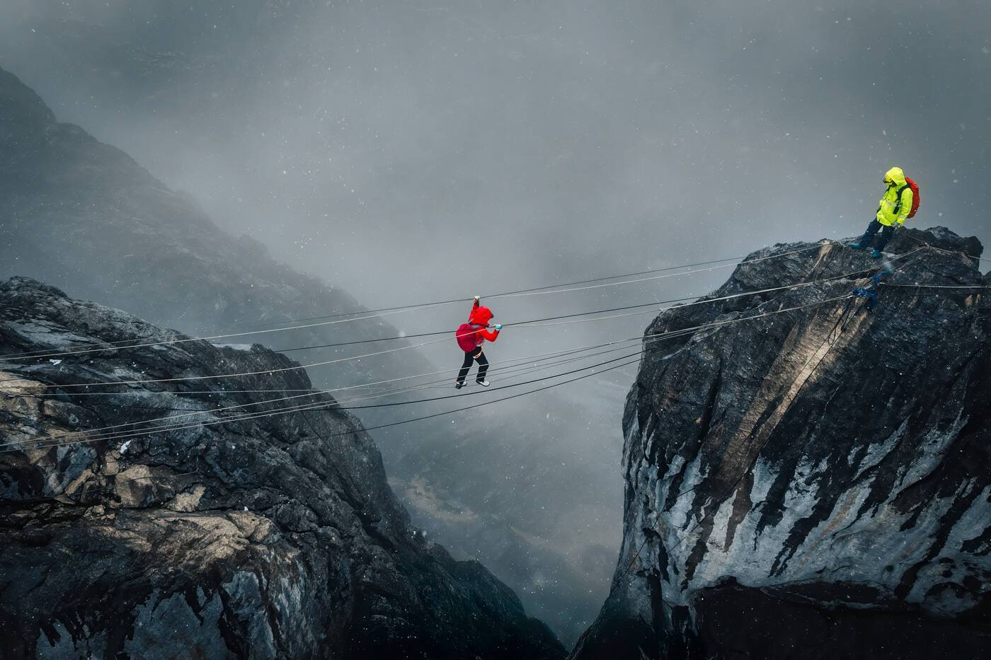 Drone shot of two climbers suspended on rope between peaks in foggy conditions
