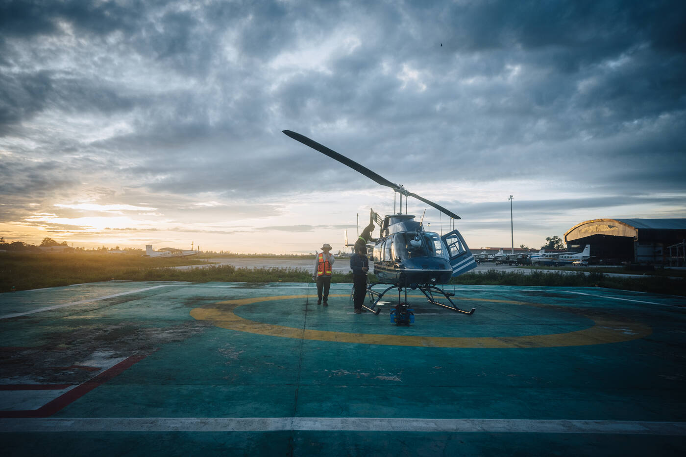 Blue helicopter on helipad in Timika at dawn with dramatic cloudy sky
